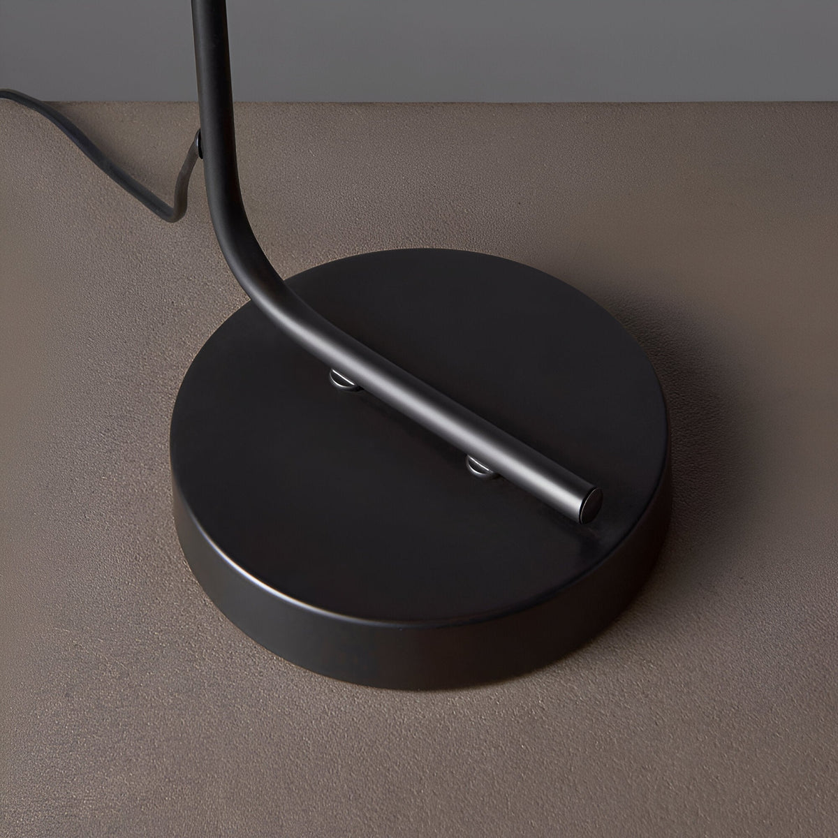 Close-up of the Endon Cranmere table lamp base, a round matt black metal disc with the curved stem rising from it and an inline switch on the flex.