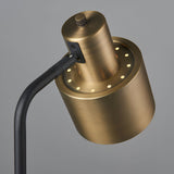 Close-up of the Carlbourne Table Lamp's antique brass cylindrical head with perforated light detailing and knurled switch, attached to a matt black bent arm.