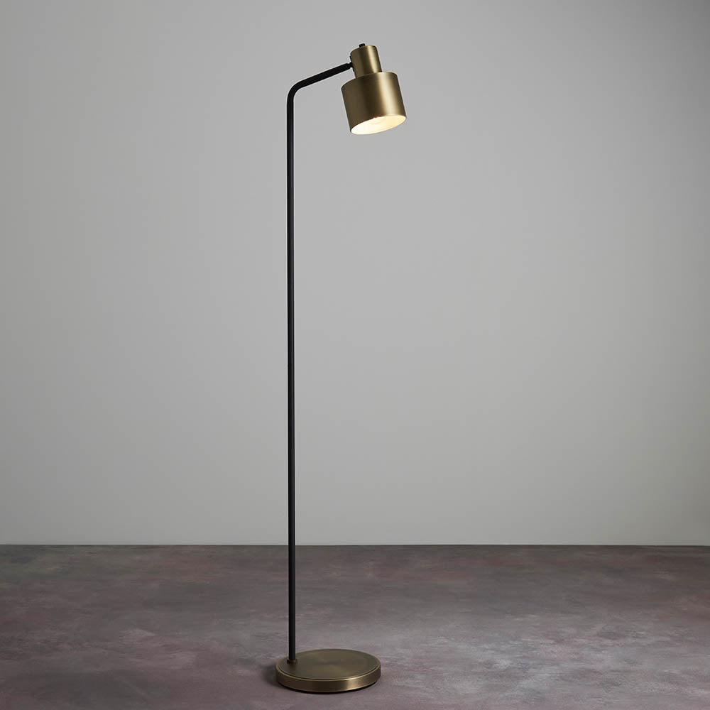 Carlbourne Floor Lamp in brass and black, tall slim frame with angled cylindrical shade on a round base, shown against a plain grey background.