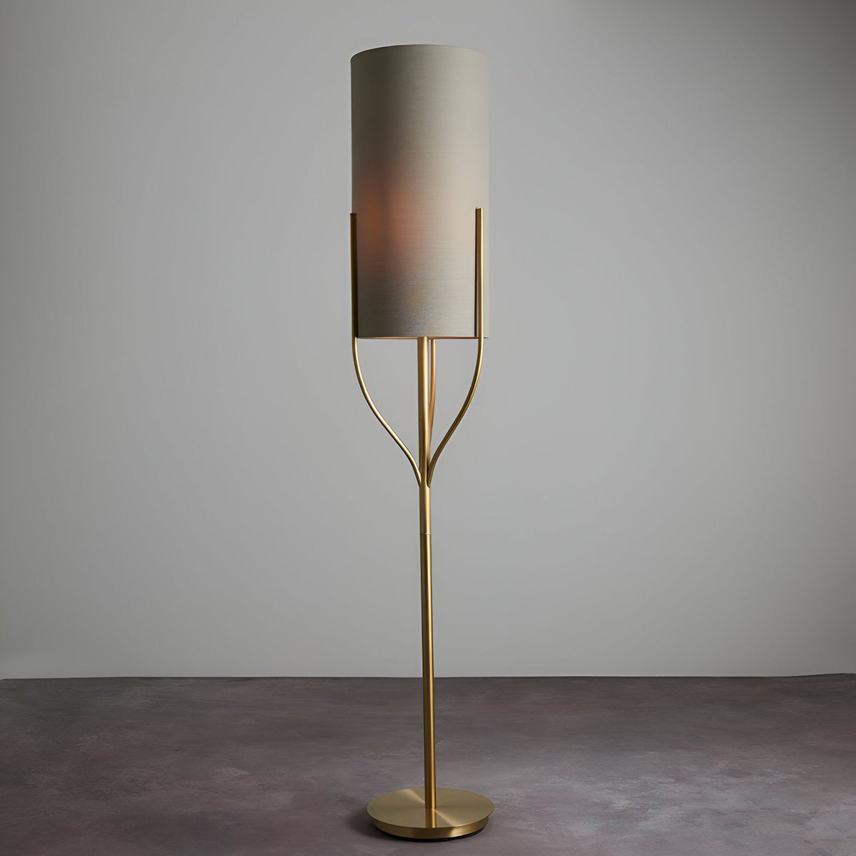 Endon Bramdon floor lamp in satin brass with a natural linen cylinder shade on a slender stem with curved supports, shown on a neutral background.