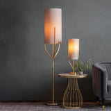 Endon Bramdon floor lamp in satin brass with tall natural linen cylinder shade, shown beside a matching table lamp on a gold side table in a living room.