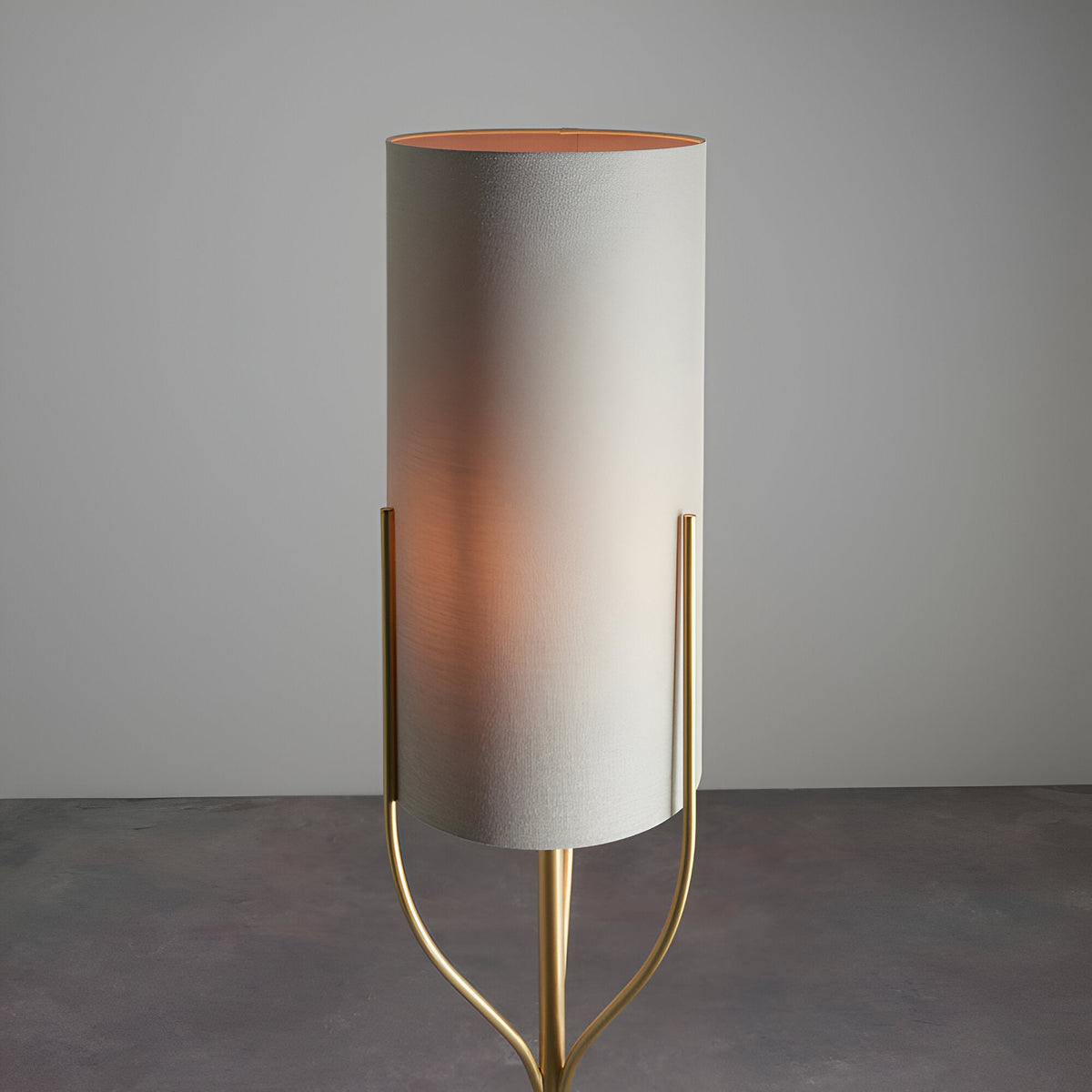 Endon Bramdon floor lamp with satin brass tripod stem and tall natural linen cylinder shade, shown illuminated against a light grey background.