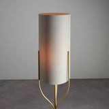 Endon Bramdon floor lamp with satin brass tripod stem and tall natural linen cylinder shade, shown illuminated against a light grey background.