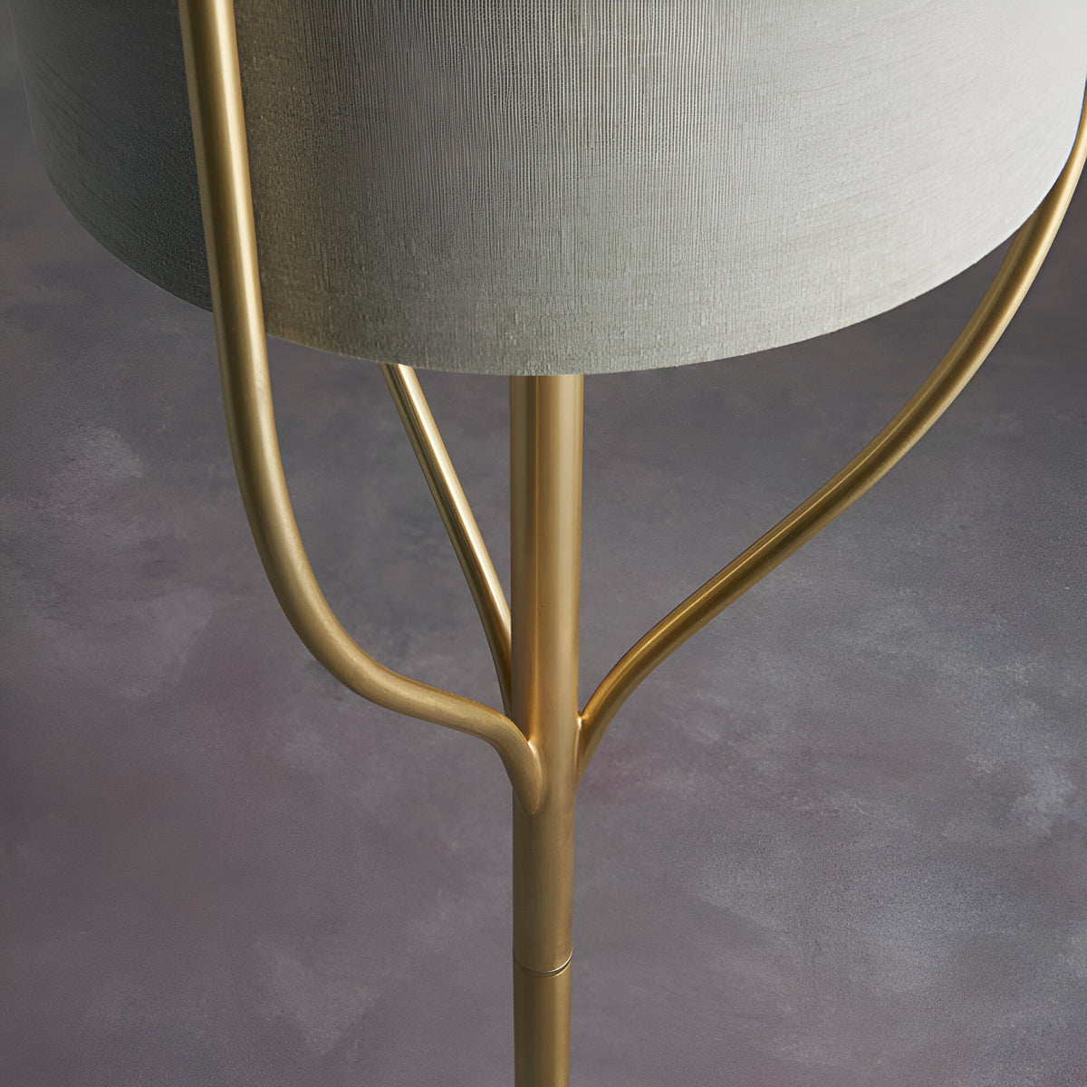 Close-up of Endon Bramdon floor lamp base showing satin brass stem with curved tripod supports and natural linen cylinder shade above.