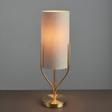 Endon Bramdon table lamp with satin brass base and slim natural linen cylinder shade, illuminated against a grey background.