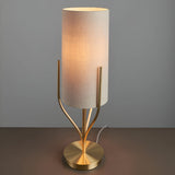 Endon Bramdon table lamp with satin brass metal base, upright branching stems, and tall natural linen cylinder shade, lit against a grey background.