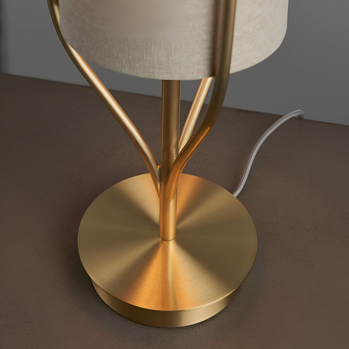 Close-up of the Endon Bramdon table lamp base, showing satin brass plated metalwork with branching stems, a round disc foot, and a natural linen shade above.