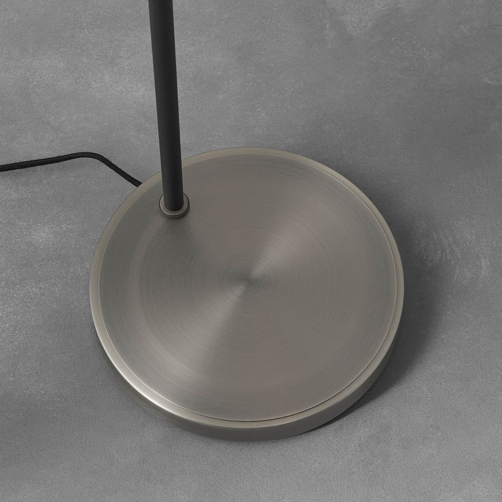 Endon Carlbourne floor lamp base close-up, showing the brushed silver circular disc and matt black stem with fabric cable, on a light grey floor.
