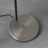 Endon Carlbourne floor lamp base close-up, showing the brushed silver circular disc and matt black stem with fabric cable, on a light grey floor.