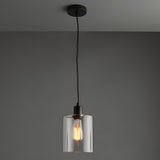 Endon Cranmere pendant light in matt black with a compact clear glass cylinder shade and exposed filament bulb on a black flex against a grey ceiling.