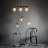 Endon Cranmere matt black pendant lights with clear glass shades, shown as a three-light bar and single drop above a side table, floor lamp and chair.