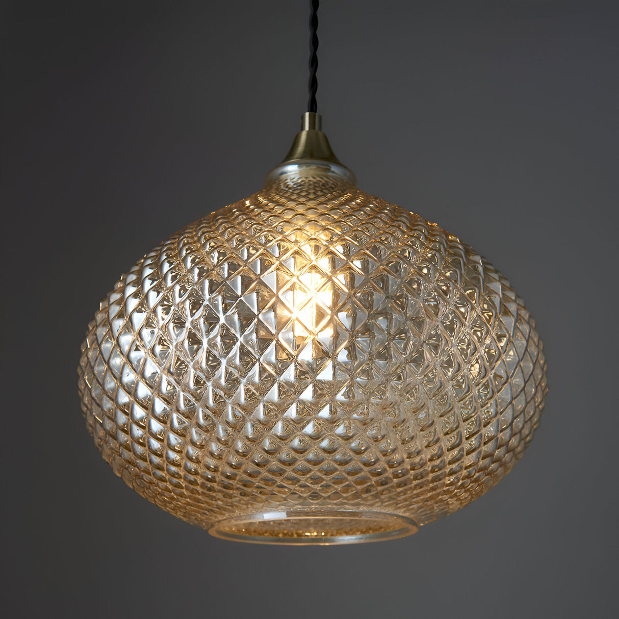 Endon Caldstead pendant light with a diamond-textured champagne glass shade on antique brass fitting and black twisted flex, against a grey background.