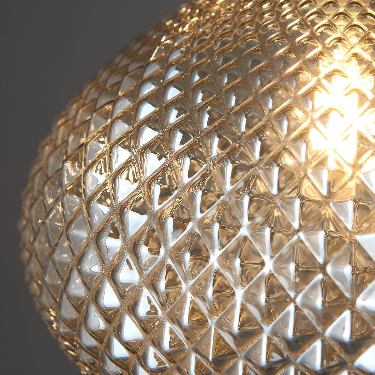 Close-up of the Endon Caldstead pendant light showing its champagne glass globe shade with diamond-cut texture, lit warmly against a grey background.
