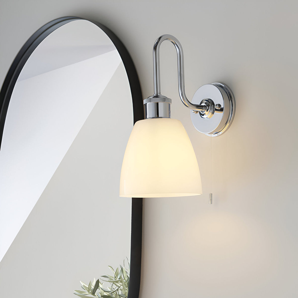 Chardon Bathroom Wall Light in polished chrome with swan-neck arm, knurled detail, opal glass shade, and pull-cord switch, beside black oval mirror.