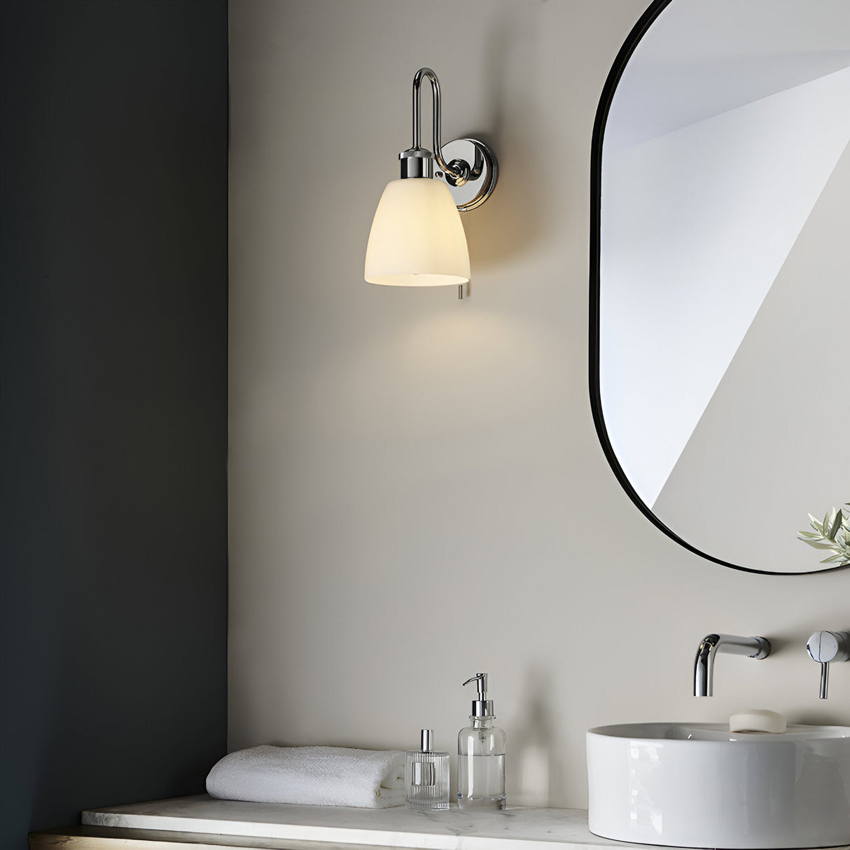 Chartdon bathroom wall light in polished chrome with a swan-neck arm and opal glass shade, shown lit beside a mirror in a neutral-toned bathroom.