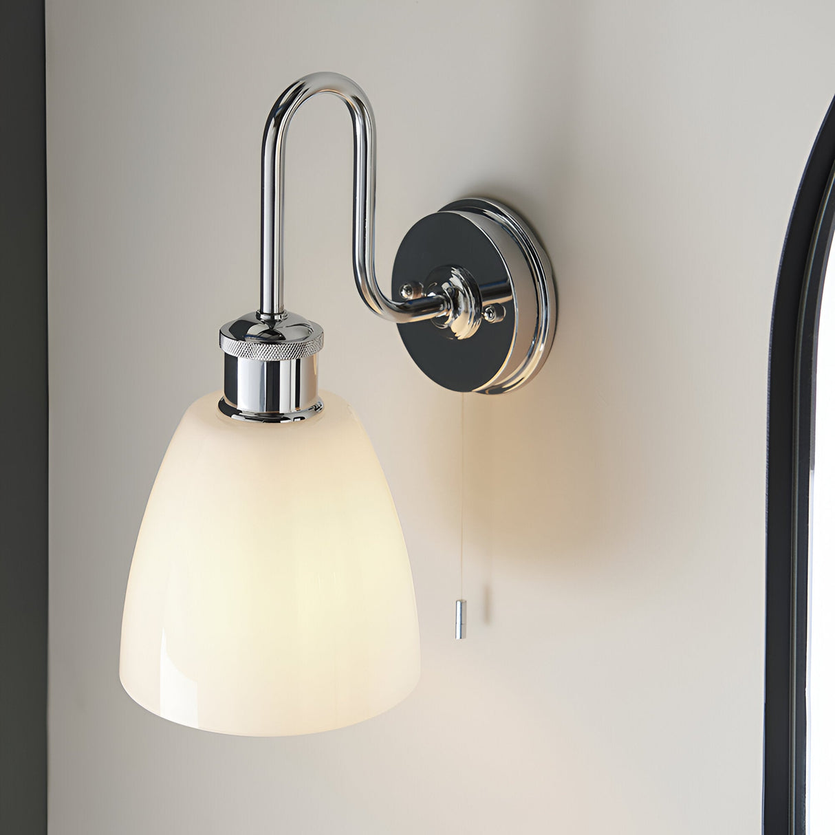 Chartdon Bathroom Wall Light in polished chrome with a swan-neck arm, knurled ring, opal glass shade, and pull-cord switch, shown mounted on a light wall.