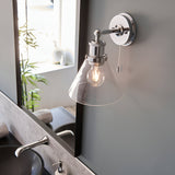 Endon Cranmore bathroom wall light in polished chrome with cone-shaped clear glass shade and pull cord, mounted beside a mirror above a basin.
