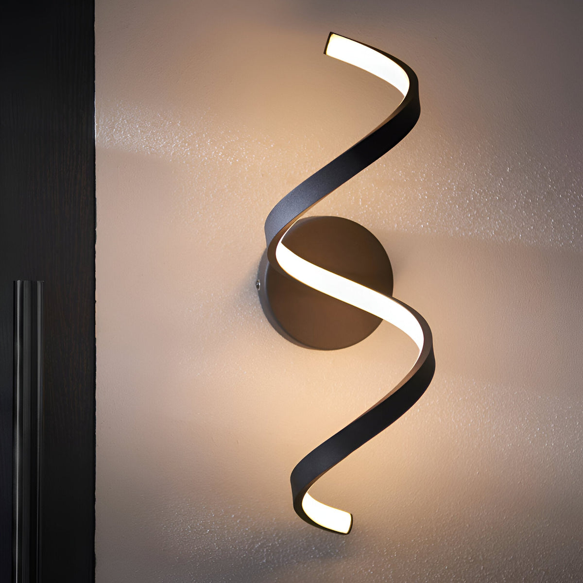 Endon Aldleigh LED wall light with a tall twisting black spiral form and warm white integrated LED, mounted on a wall beside a dark door frame.
