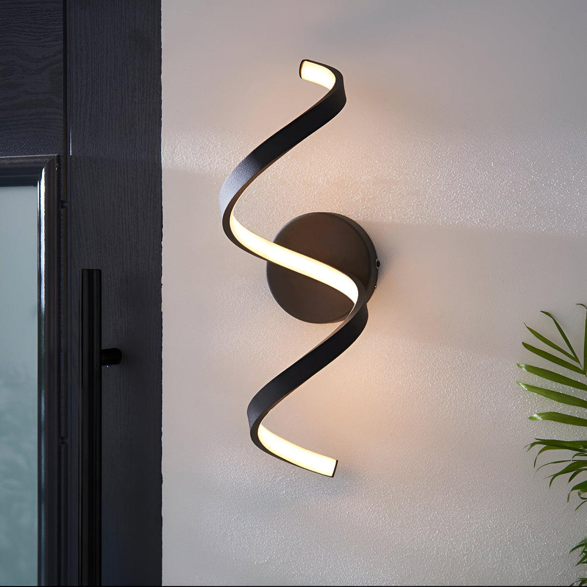 Endon Aldleigh LED wall light in black with a tall twisting spiral form emitting warm white light, mounted beside a dark framed glass door.