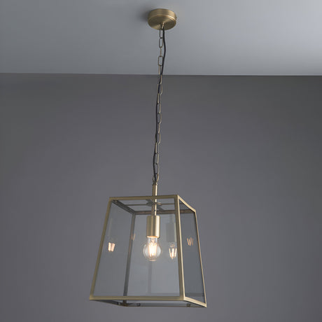 Endon Brenton lantern pendant in brass with tapered metal frame, clear glass panels and filament bulb, suspended from a chain against a grey ceiling.
