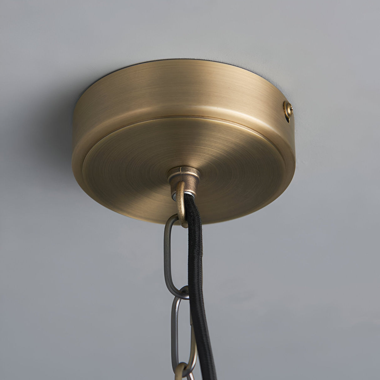 Close-up of the Endon Brenton pendant's brass ceiling rose with black fabric flex and chain suspension against a light grey ceiling.