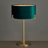 Brendon Table Lamp in matt antique brass with a green velvet drum shade on a slender stem base, shown against a plain grey background.