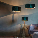 Brendon Table Lamp in brass with green velvet drum shade, shown on a side table beside a floor lamp and pendant light in a living room setting.