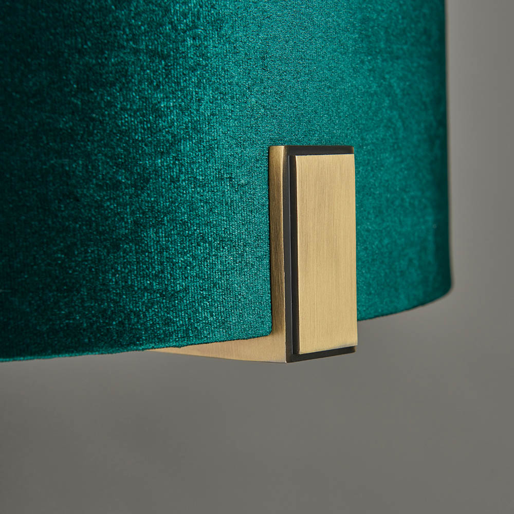 Close-up of the Brendon Table Lamp's green velvet shade edge and matt antique brass bracket, on a plain grey background.