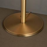 Close-up of the Brendon Table Lamp's round, matt antique brass base and stem, showing brushed metal texture on a light surface.