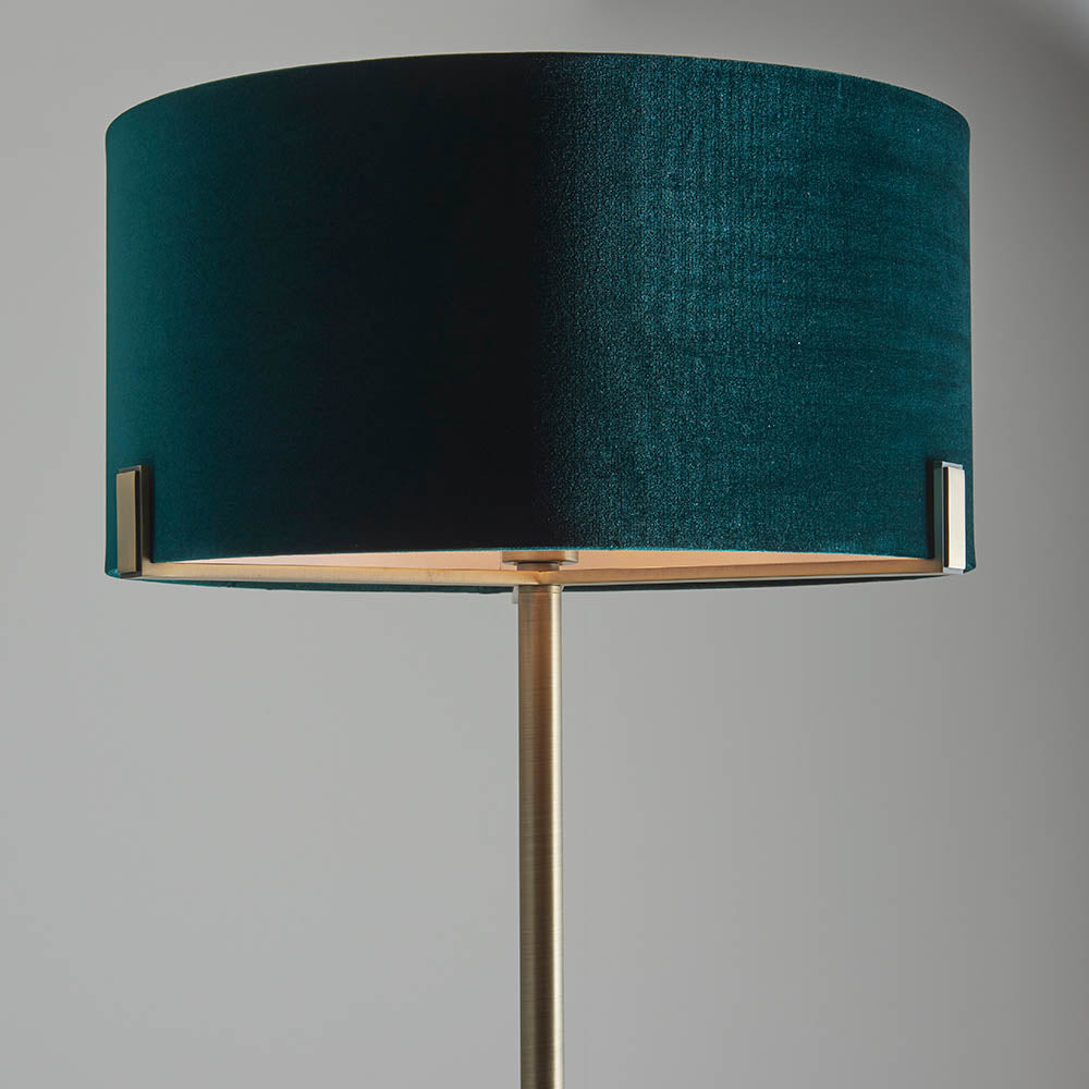 Endon Brendon floor lamp shown close-up with a green velvet cylinder shade held on slim antique brass metalwork against a light grey background.