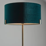 Endon Brendon floor lamp shown close-up with a green velvet cylinder shade held on slim antique brass metalwork against a light grey background.