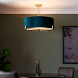 Brendon 3 Light Pendant in brass with a teal green drum shade and white diffuser, hung above a dining table in a green-walled room.