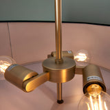 Close-up of the Brendon 3 Light Pendant's brass fitting with three angled arms holding exposed E27 bulbs beneath a pale pink fabric shade.