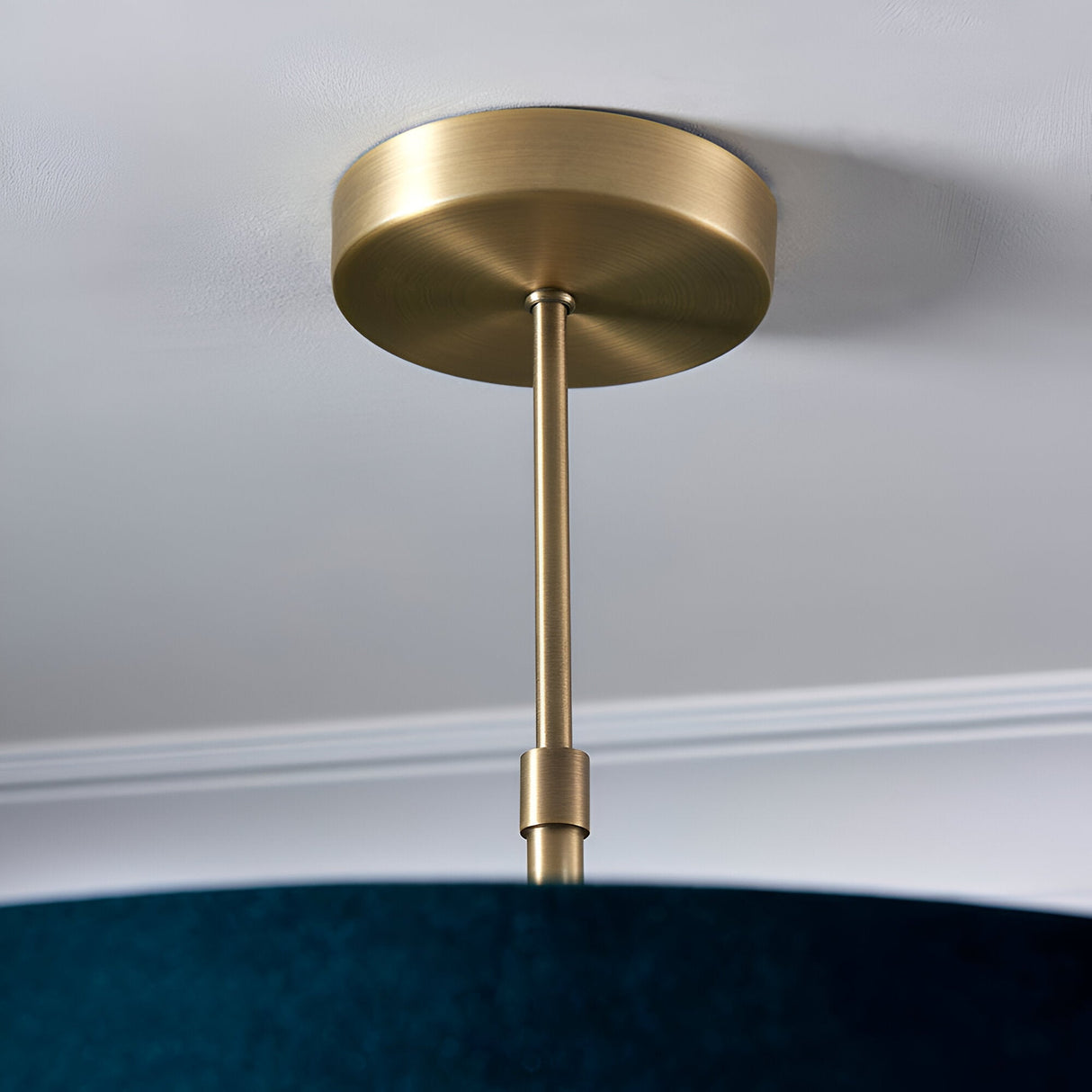 Brendon 3 Light Pendant close-up showing brushed brass ceiling mount and telescopic stem, with green fabric shade edge visible below.