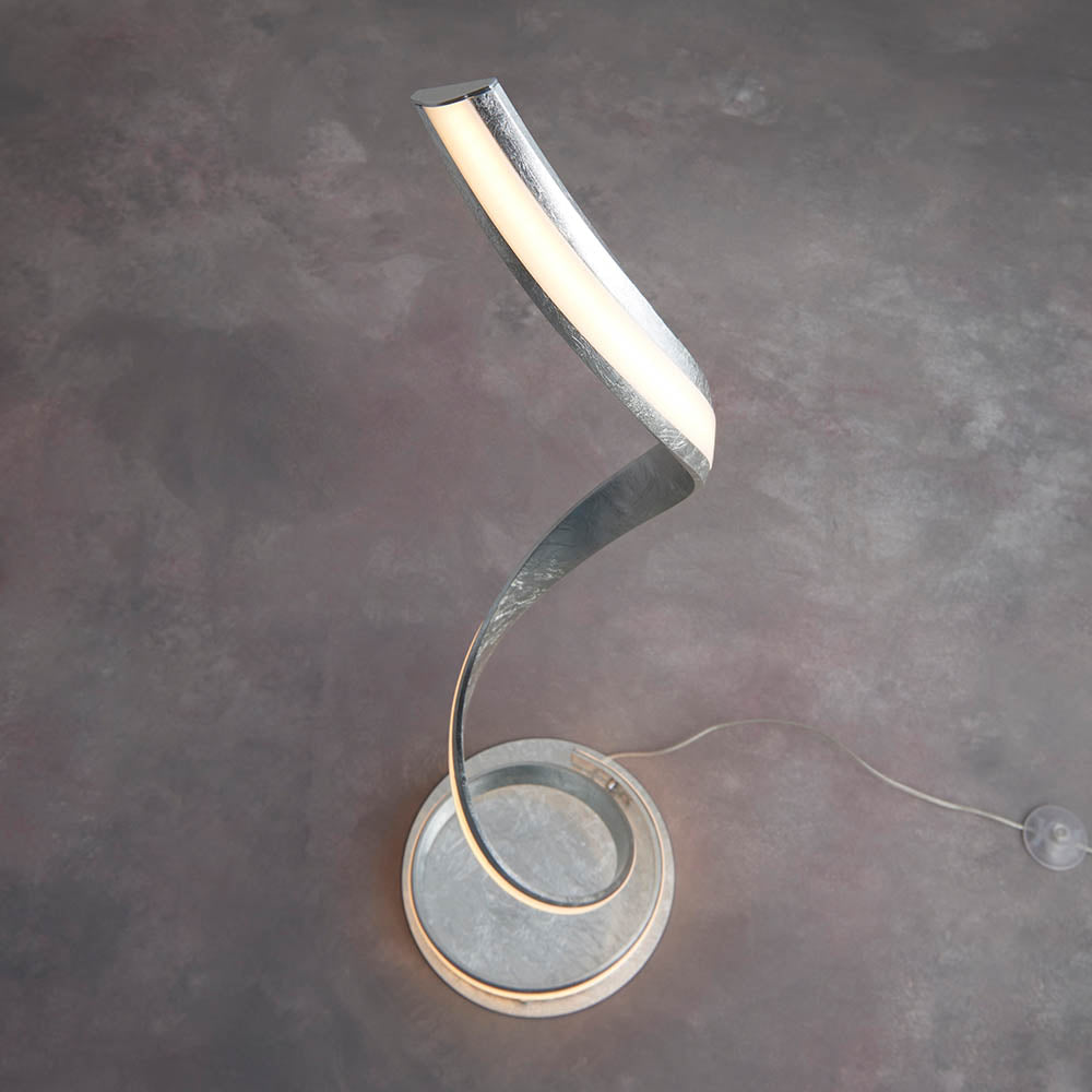 Endon Neve LED floor lamp with a spiralling silver leaf curve and white diffuser, mounted on a round base with in-line cable on a grey floor.