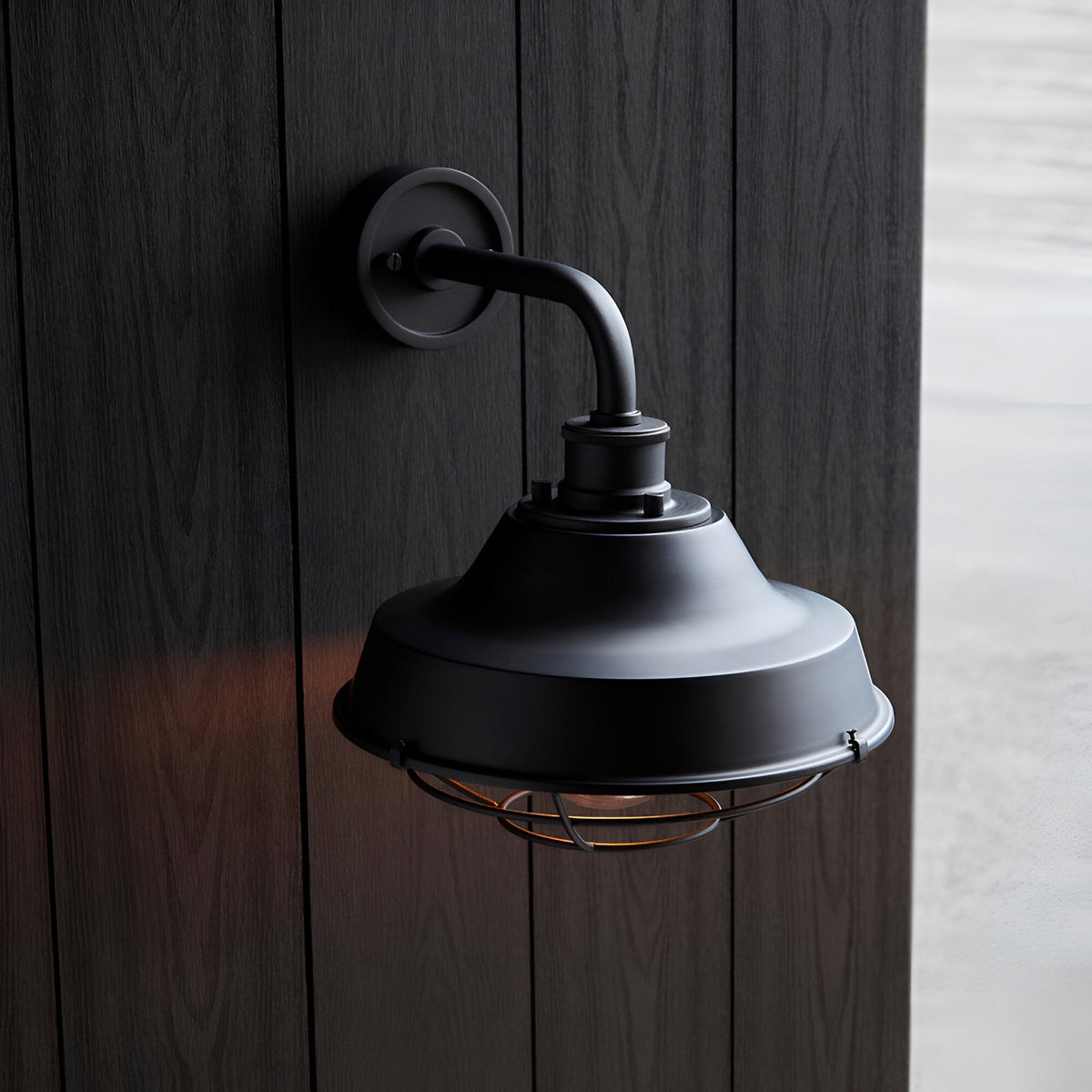 Caldton Outdoor Wall Light in matt black, industrial-style with protective cage shade, mounted on dark wood panelling wall.