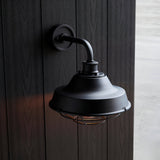 Caldton Outdoor Wall Light in matt black, industrial-style with protective cage shade, mounted on dark wood panelling wall.