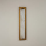 Valora vertical wall light with a tall natural alabaster panel in a brushed brass rectangular frame, mounted on a plain light background.