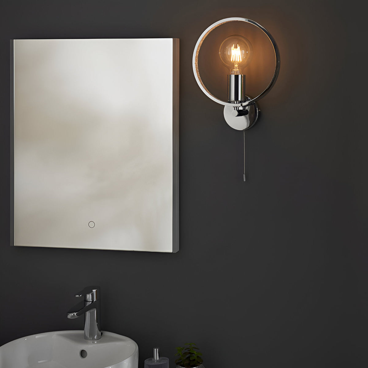 Endon Carlcombe chrome bathroom wall light with faceted ring, E27 globe bulb and pull cord, mounted beside a rectangular LED mirror above a basin.