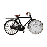 Black metal miniature pedal bike mantel clock with silver spokes, handlebars and cranks, brown saddle and grips, and a white clock face in the front wheel.