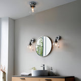 Endon Tarn flush bathroom ceiling light in chrome with a clear glass globe shade, shown above a round mirror and twin wall lights over a vanity.