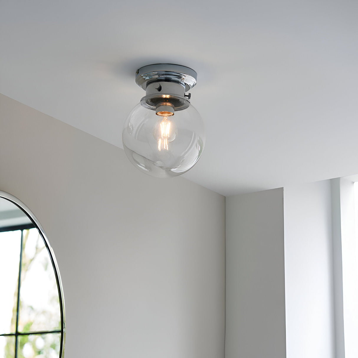 Endon Tarn flush bathroom ceiling light with a clear glass globe shade and chrome fitting, mounted on a white ceiling beside an arched mirror.