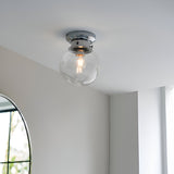 Endon Tarn flush bathroom ceiling light with a clear glass globe shade and chrome fitting, mounted on a white ceiling beside an arched mirror.