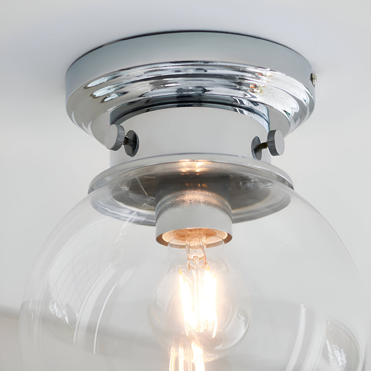 Endon Tarn flush bathroom ceiling light in chrome with a clear glass globe shade and single illuminated E27 lamp, shown close-up against a white ceiling.