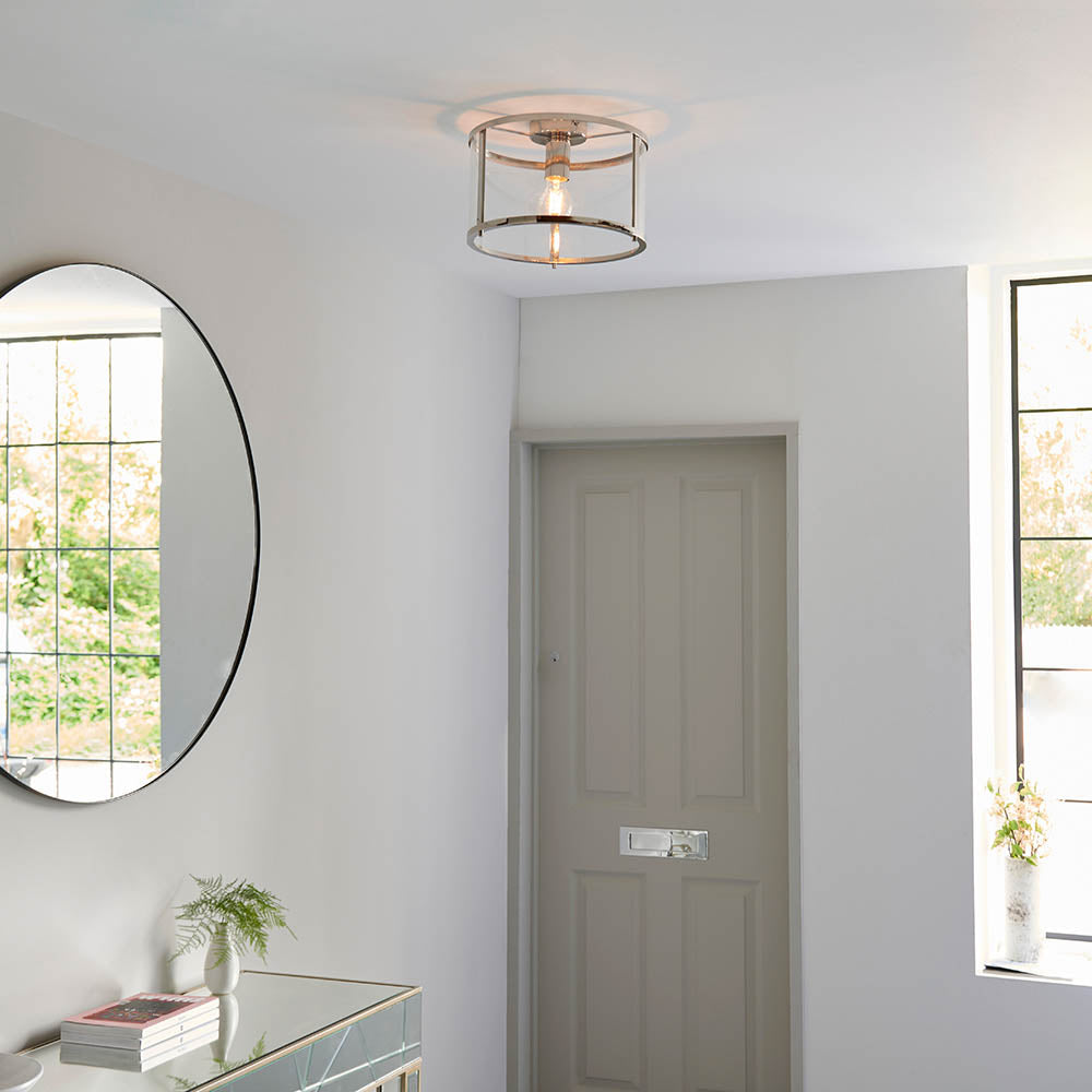 Endon Ellery brushed nickel flush ceiling light with cylindrical glass shade and exposed E27 bulb, fitted in a bright hallway with round mirror and door.