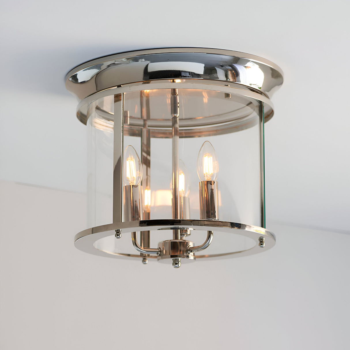 Endon Hollis 3 light flush ceiling light in nickel with cylindrical clear glass shade and three E14 candle lamps, mounted to a white ceiling.