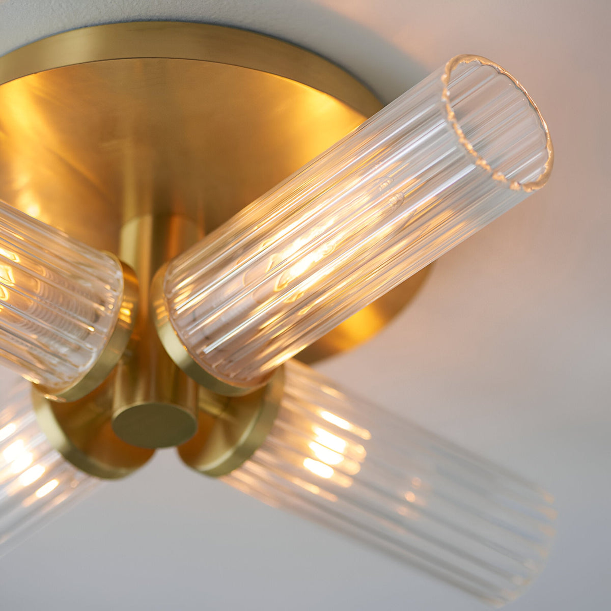 Close-up of Endon Wren 4 light semi-flush bathroom ceiling light in brass, showing ribbed glass cylinder shades on angled arms beneath a circular plate.