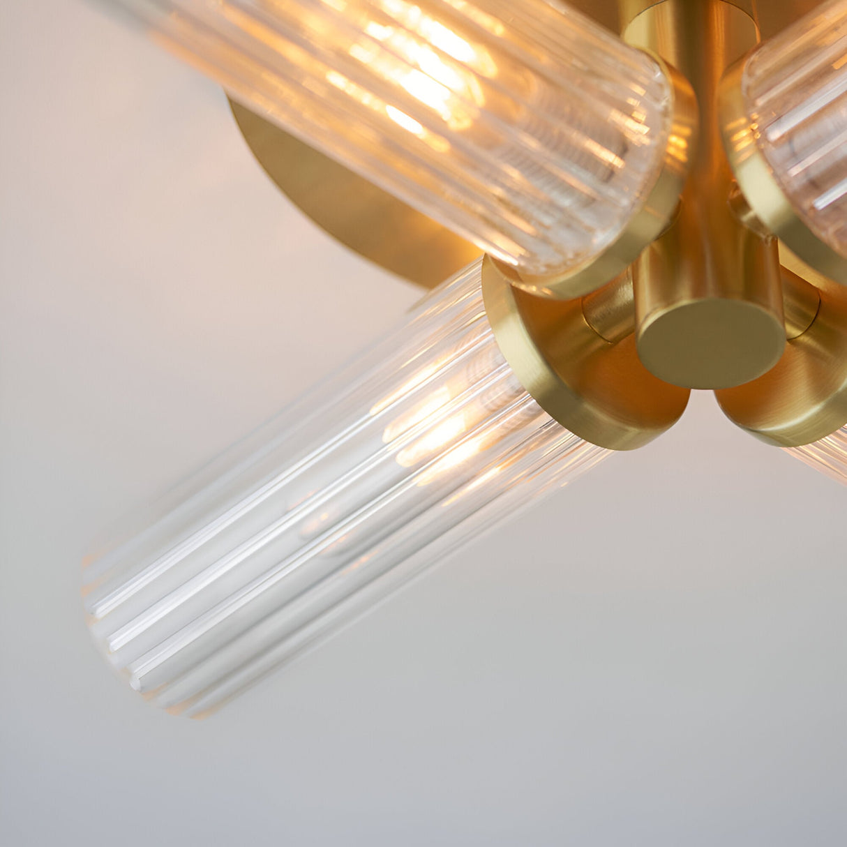 Close-up of the Endon Wren semi-flush bathroom ceiling light showing brushed brass arms and fluted clear glass cylindrical shades with lit G9 lamps.
