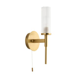 Endon Wren bathroom wall light in satin brass with a clear ribbed cylindrical glass shade, pull switch and round backplate, on a white background.