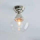 Endon Kedleston semi-flush ceiling light with polished nickel mount and clear glass schoolhouse shade, single E27 bulb lit, mounted on a white ceiling.